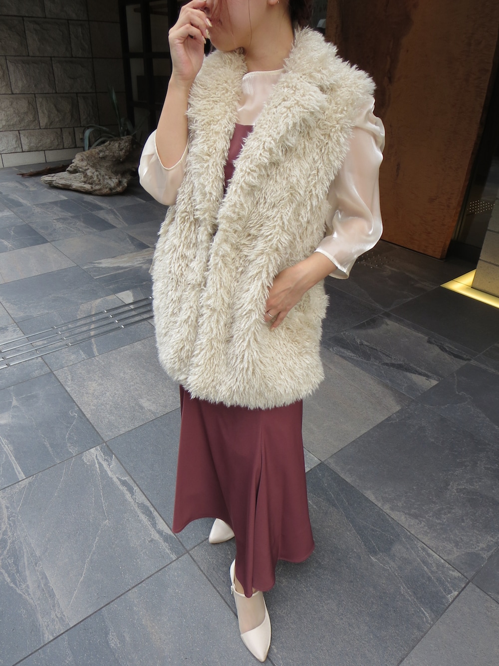 レッド系のドレス、ベージュ系のベスト、ベージュ系のブーツを着用したレディースの秋コーディネートの2枚目の写真