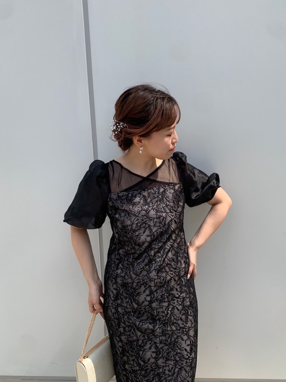 ブラック系のドレス、ブラック系のクラッチバッグ、ベージュ系のパンプスを着用したレディースの春コーディネートの3枚目の写真