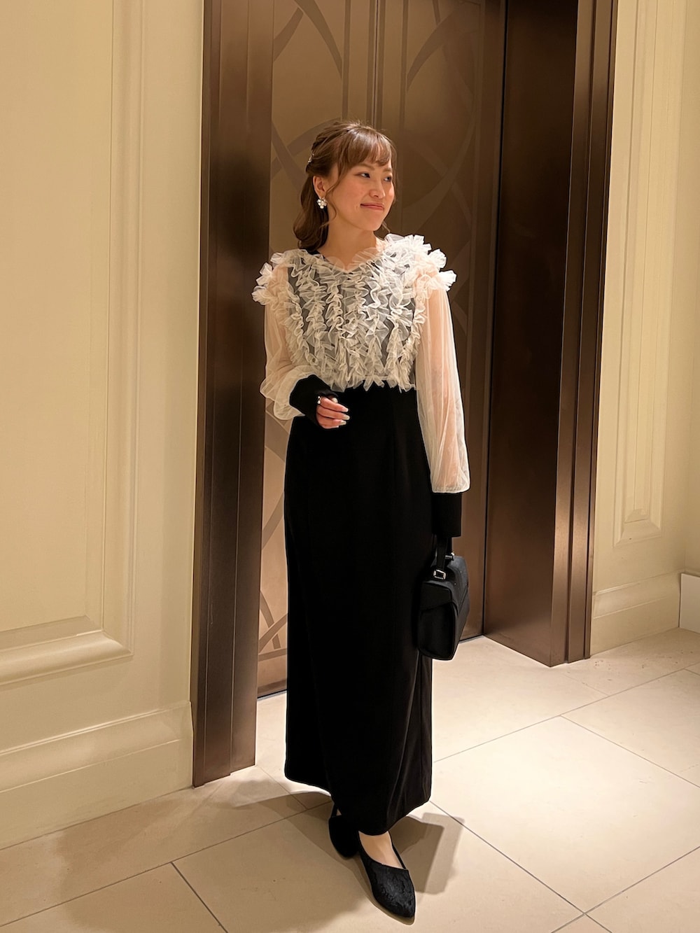 ブラック系のドレス、ブラック系のハンドバッグ、ゴールド系のヘアピンを着用したレディースの春コーディネートの2枚目の写真