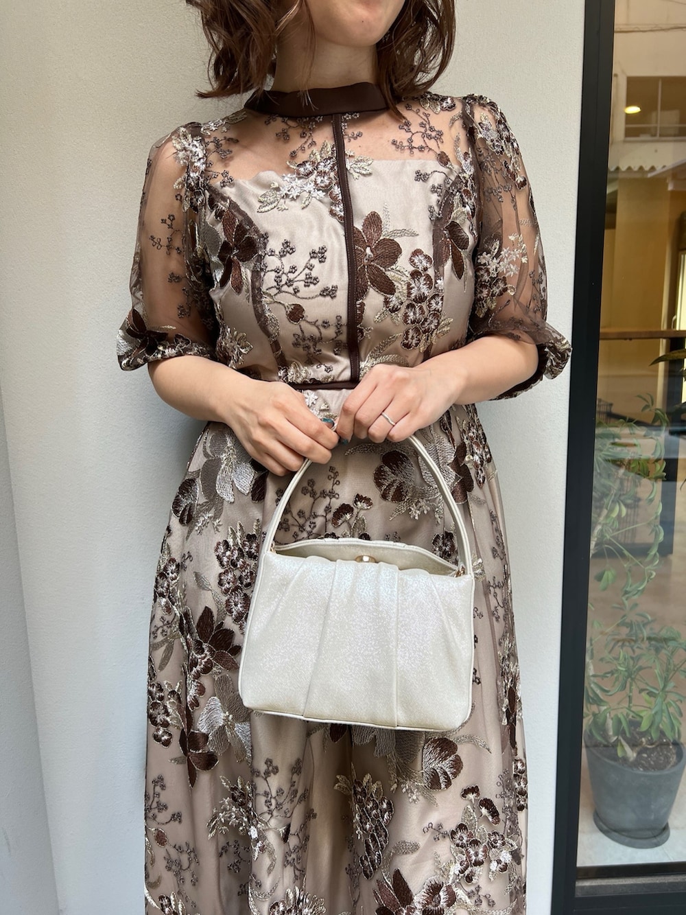 ブラウン系のドレス、ベージュ系のハンドバッグを着用したレディースの春コーディネートの2枚目の写真
