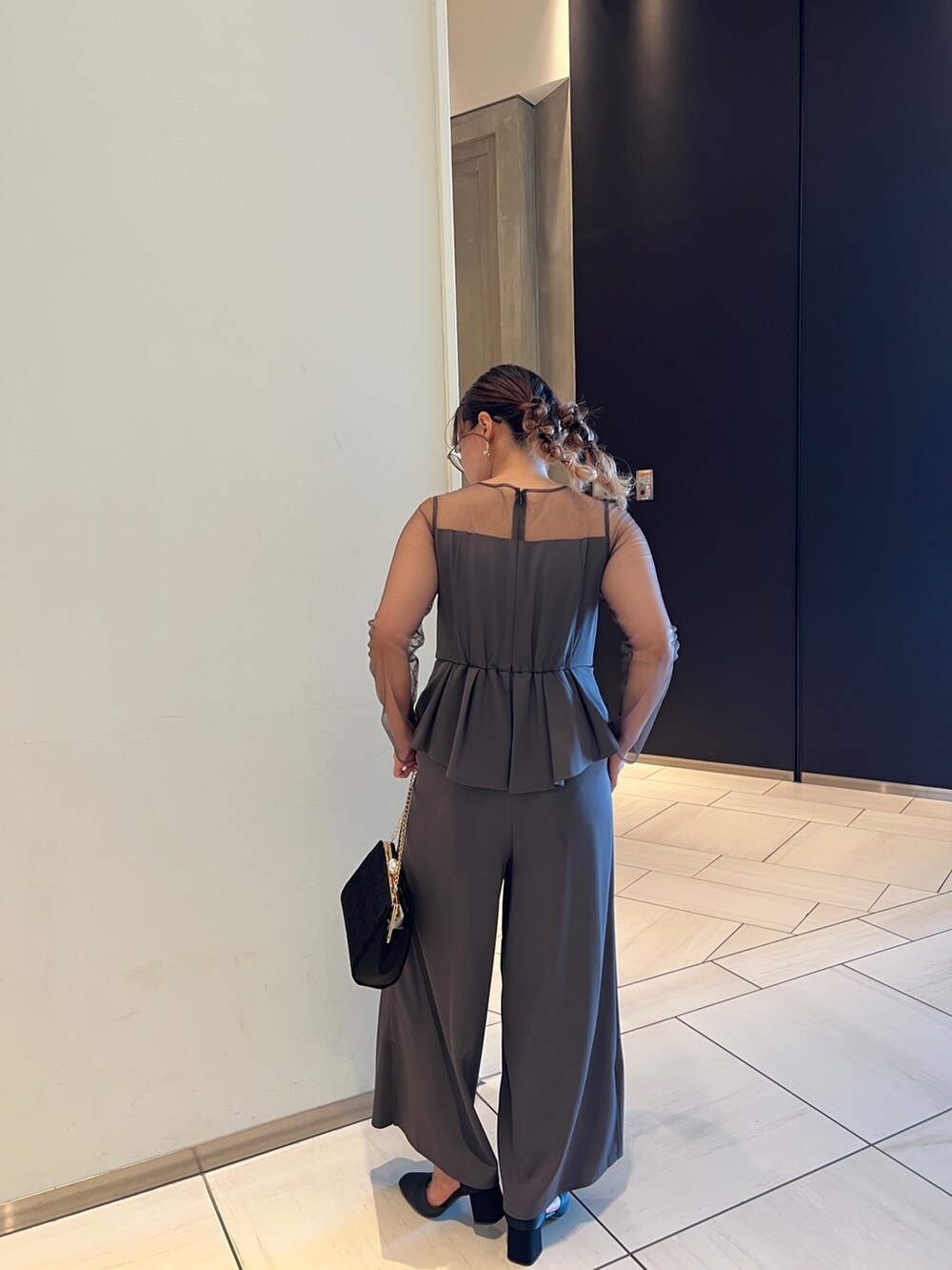 グレー系のパンツドレス、ブラック系のクラッチバッグ、ブラック系のパンプスを着用したレディースの秋コーディネートの6枚目の写真