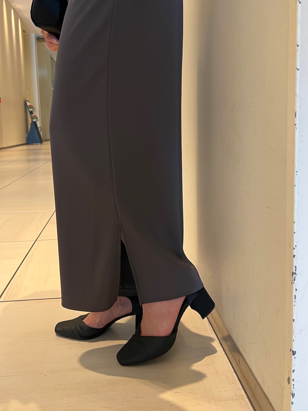 グレー系のパンツドレス、ブラック系のクラッチバッグ、ブラック系のパンプスを着用したレディースの秋コーディネートの7枚目の写真