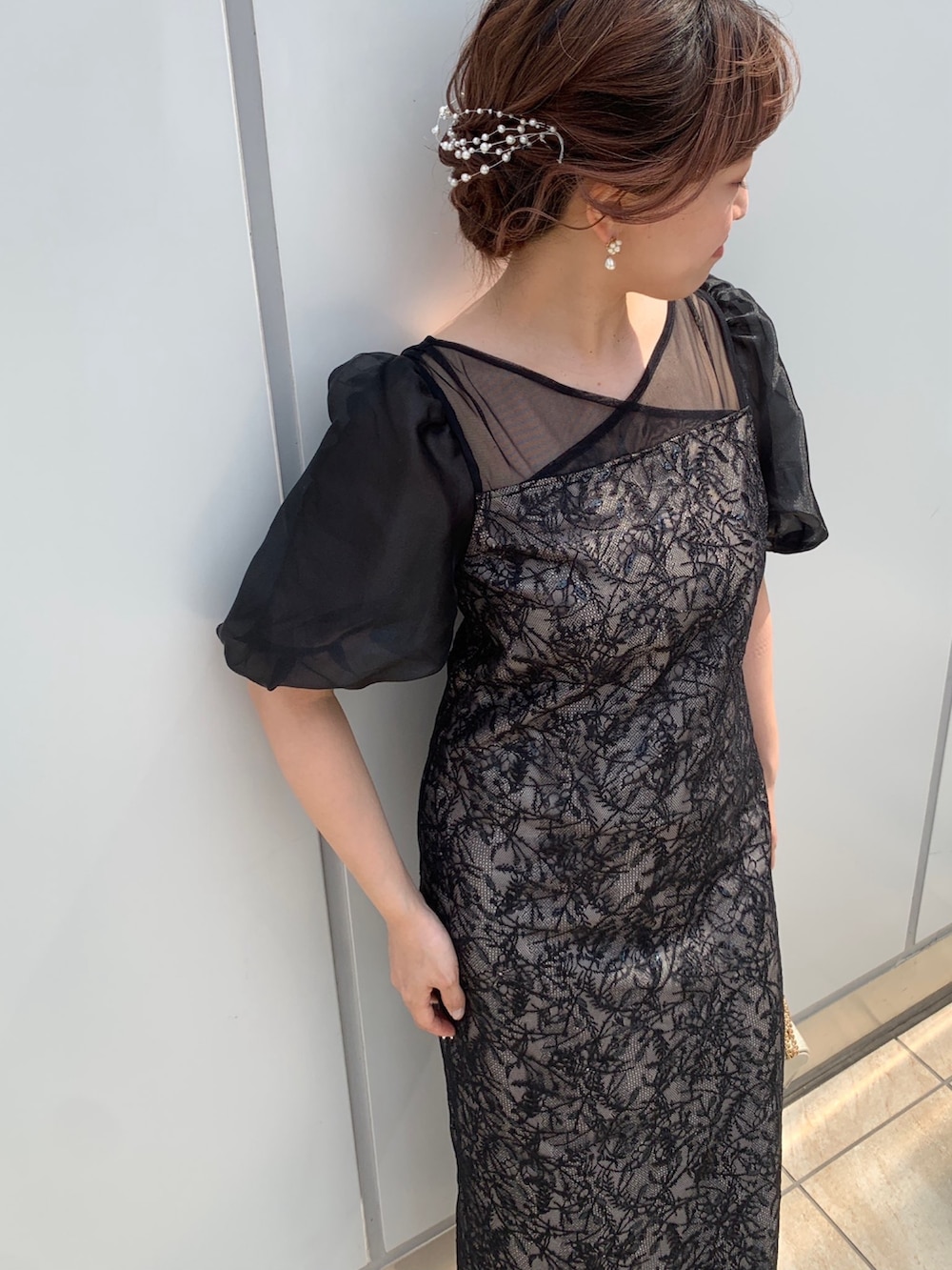 ブラック系のドレス、ブラック系のクラッチバッグ、ベージュ系のパンプスを着用したレディースの春コーディネートの5枚目の写真