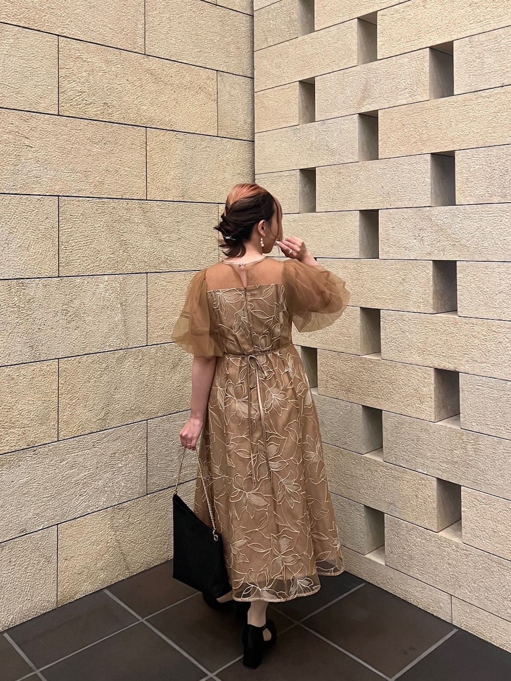 オレンジ系のドレス、ブラック系のパンプス、ブラック系のショルダーバッグを着用したレディースの春コーディネートの6枚目の写真