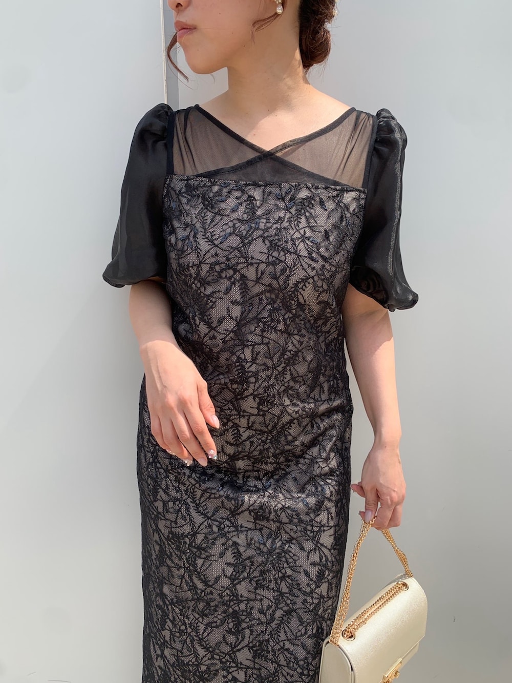 ブラック系のドレス、ブラック系のクラッチバッグ、ベージュ系のパンプスを着用したレディースの春コーディネートの4枚目の写真