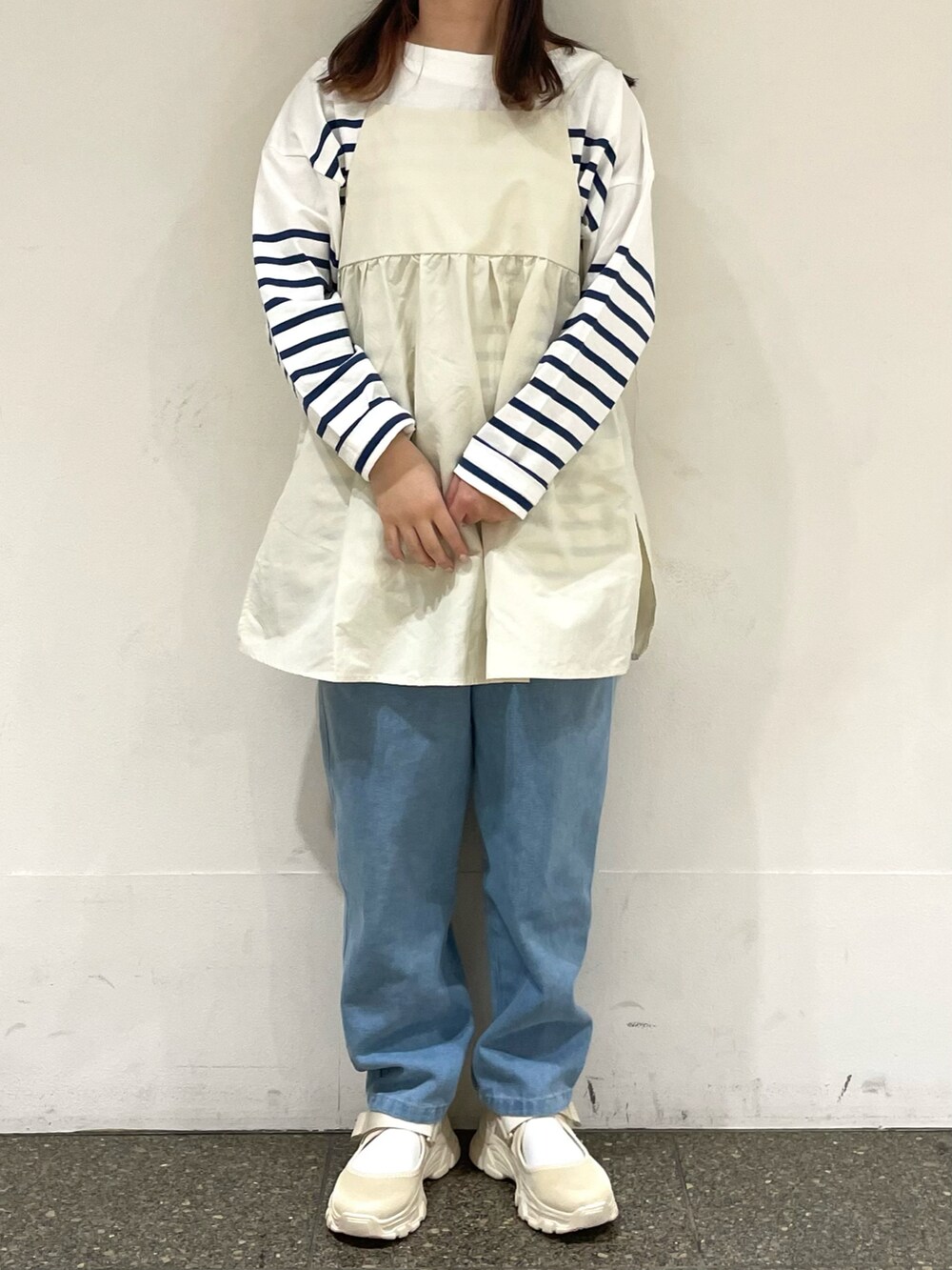 ベージュ系のスニーカー、ホワイト系のチュニック、ブルー系のデニムパンツを着用したレディースの春コーディネートの2枚目の写真