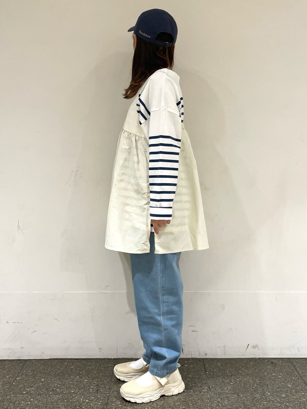 ベージュ系のスニーカー、ホワイト系のチュニック、ブルー系のデニムパンツを着用したレディースの春コーディネートの3枚目の写真