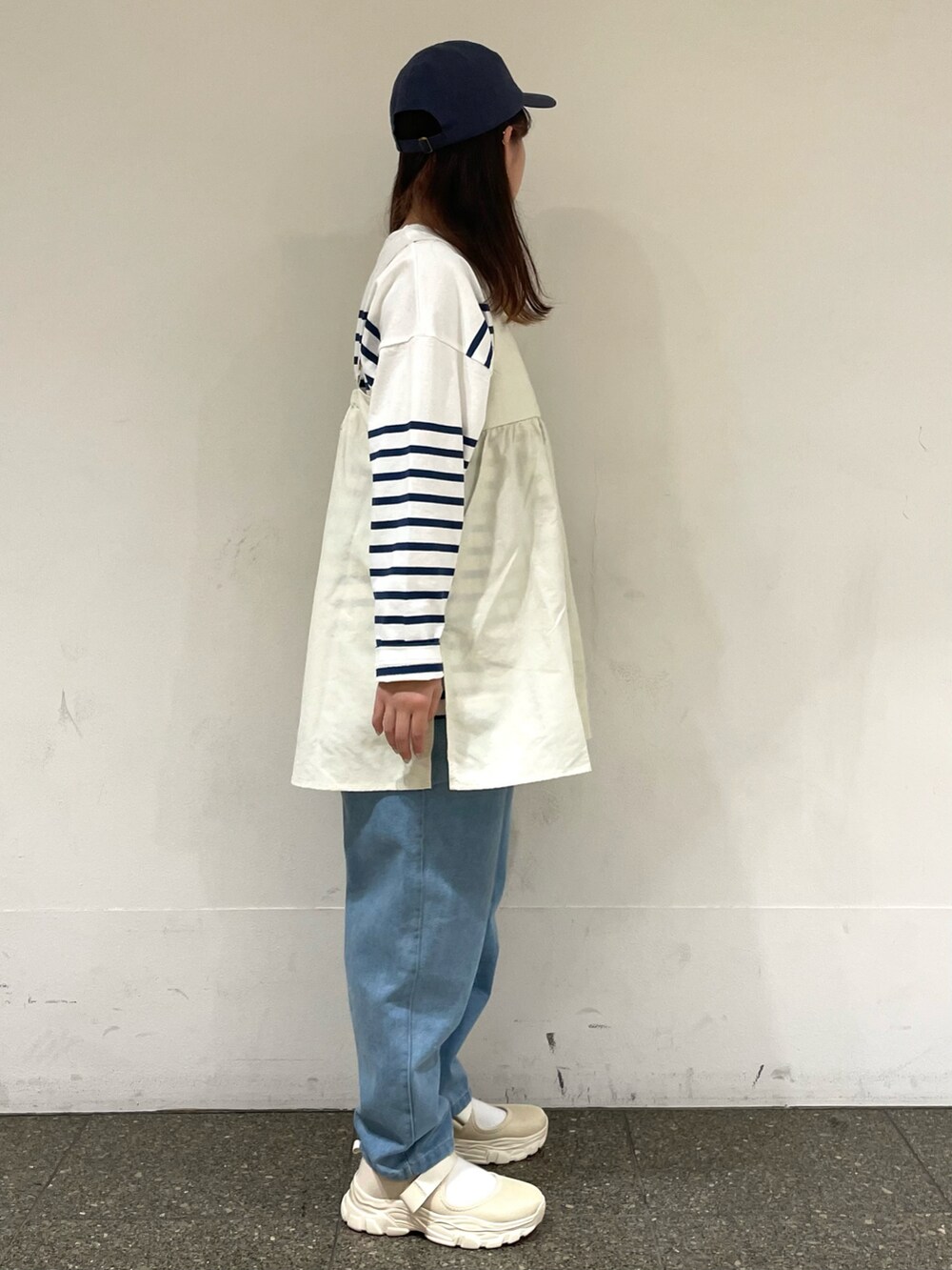 ベージュ系のスニーカー、ホワイト系のチュニック、ブルー系のデニムパンツを着用したレディースの春コーディネートの5枚目の写真