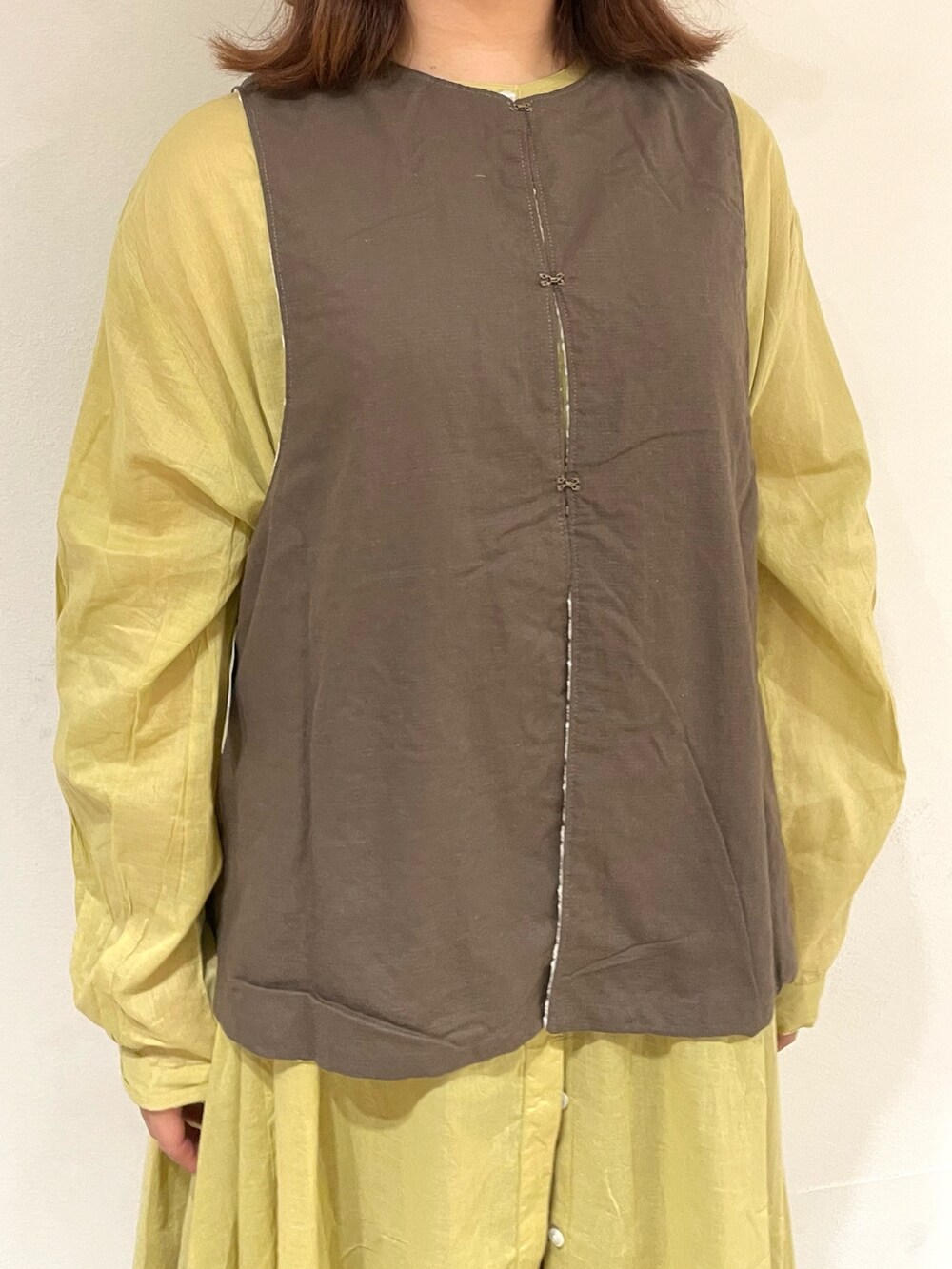 ホワイト系のベスト、イエロー系のワンピース、ブラウン系のスカートを着用したレディースの夏コーディネートの4枚目の写真