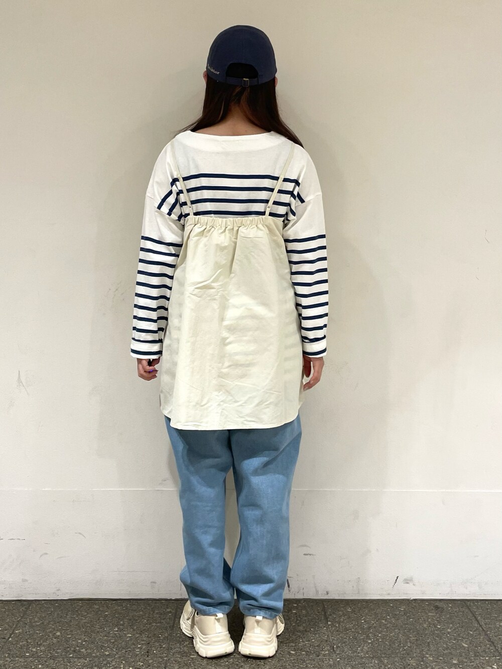 ベージュ系のスニーカー、ホワイト系のチュニック、ブルー系のデニムパンツを着用したレディースの春コーディネートの4枚目の写真