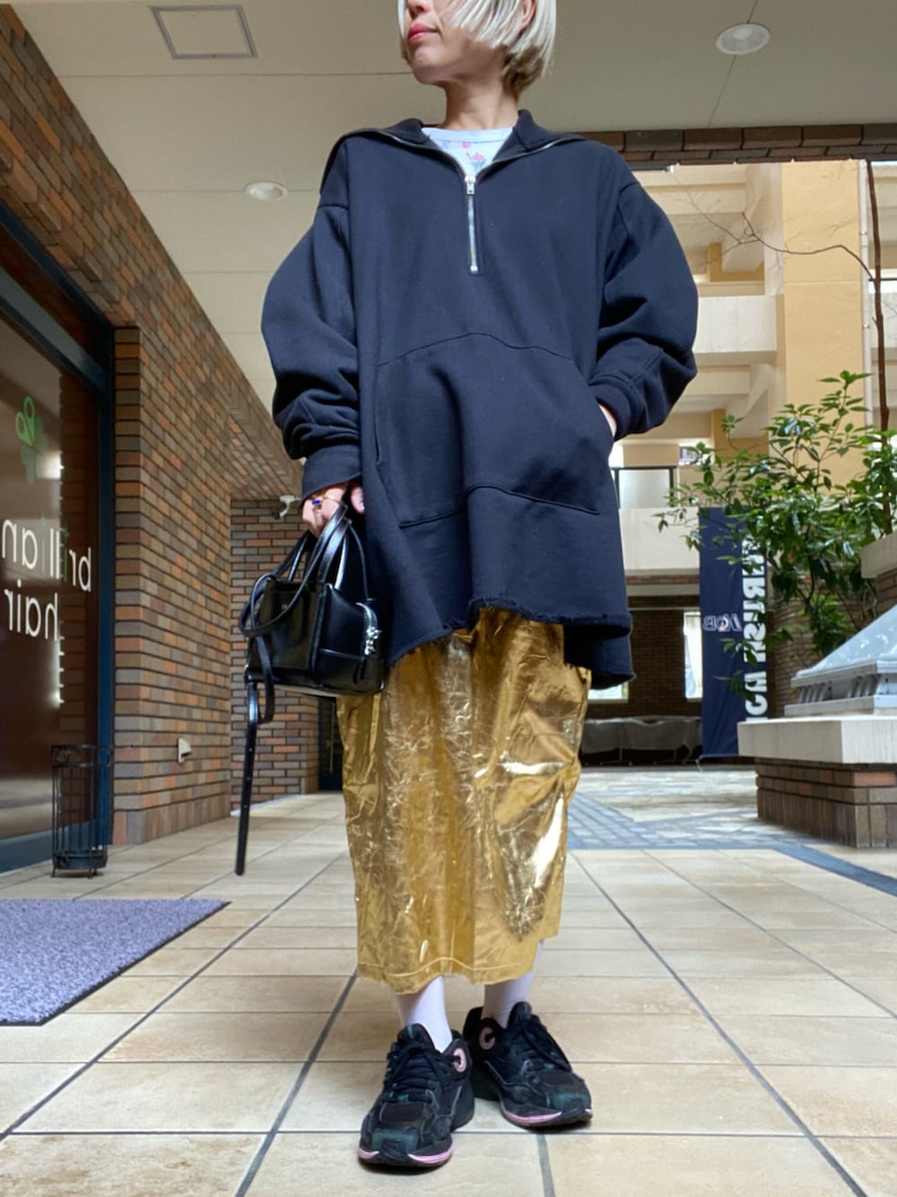 ゴールド系のスカート、ブラック系のスニーカー、グリーン系のブルゾンを着用したレディースの春コーディネートの2枚目の写真