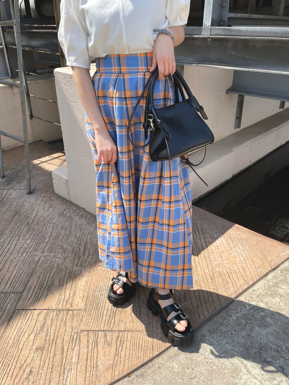 ブルー系のスカート、ブラック系のショルダーバッグ、ホワイト系のTシャツ/カットソーを着用したレディースの夏コーディネートの2枚目の写真