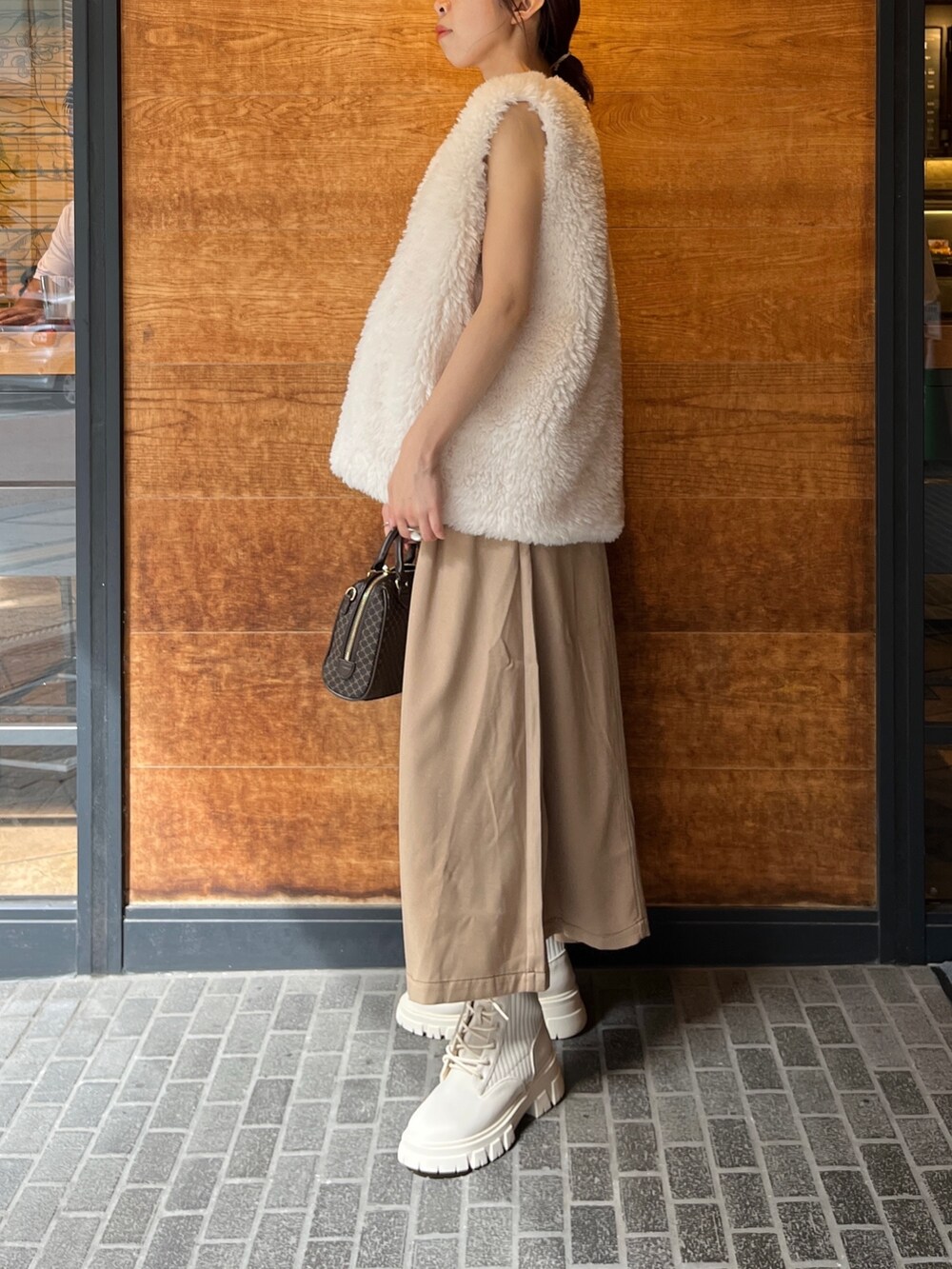 ブラウン系のボストンバッグ、ベージュ系のワンピース、ホワイト系のベストを着用したレディースの秋コーディネートの2枚目の写真