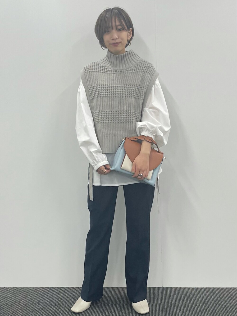 ブルー系のスラックス、ブルー系のトートバッグ、ゴールド系のピアス（両耳用）を着用したレディースの冬コーディネートの2枚目の写真