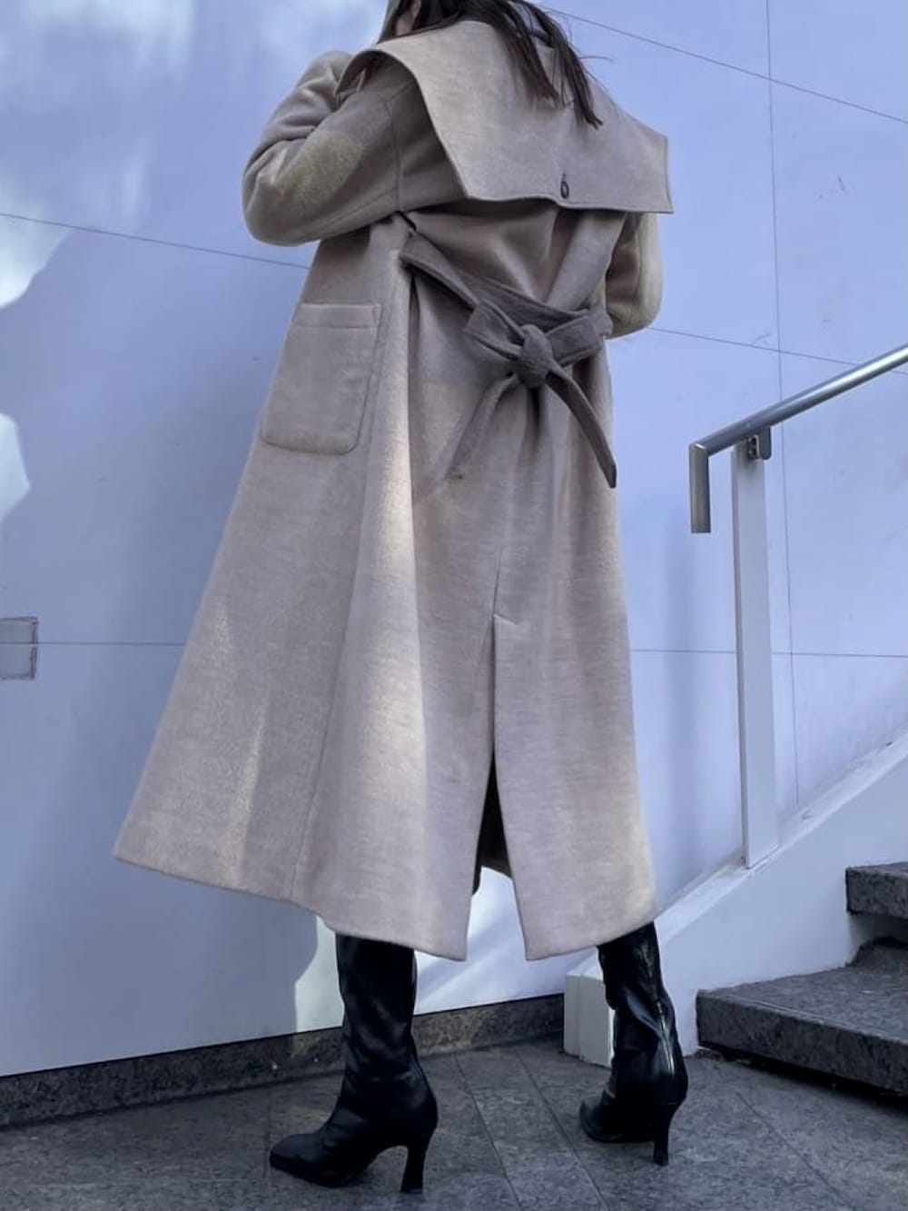 グレー系のスカート、ブルー系のニット/セーター、ベージュ系のステンカラーコートを着用したレディースの冬コーディネートの2枚目の写真