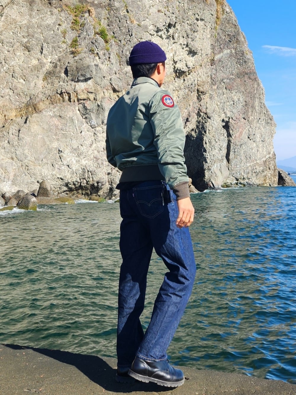 グリーン系のミリタリージャケット、ブラック系のその他トップス、ブルー系のデニムパンツを着用したメンズの秋コーディネートの3枚目の写真