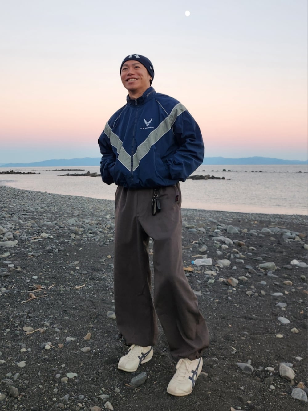 ブルー系のナイロンジャケット、グレー系のスラックス、ホワイト系のスニーカーを着用したメンズの秋コーディネートの2枚目の写真