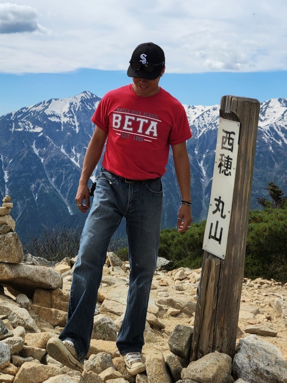 レッド系のTシャツ/カットソー、ブルー系のデニムパンツ、ベージュ系のスニーカーを着用したメンズの春コーディネートの2枚目の写真