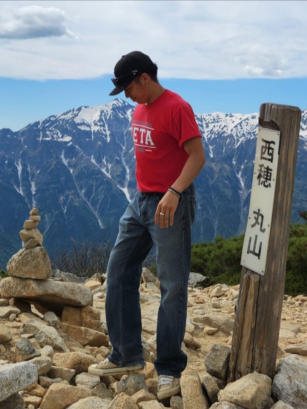 レッド系のTシャツ/カットソー、ブルー系のデニムパンツ、ベージュ系のスニーカーを着用したメンズの春コーディネートの3枚目の写真