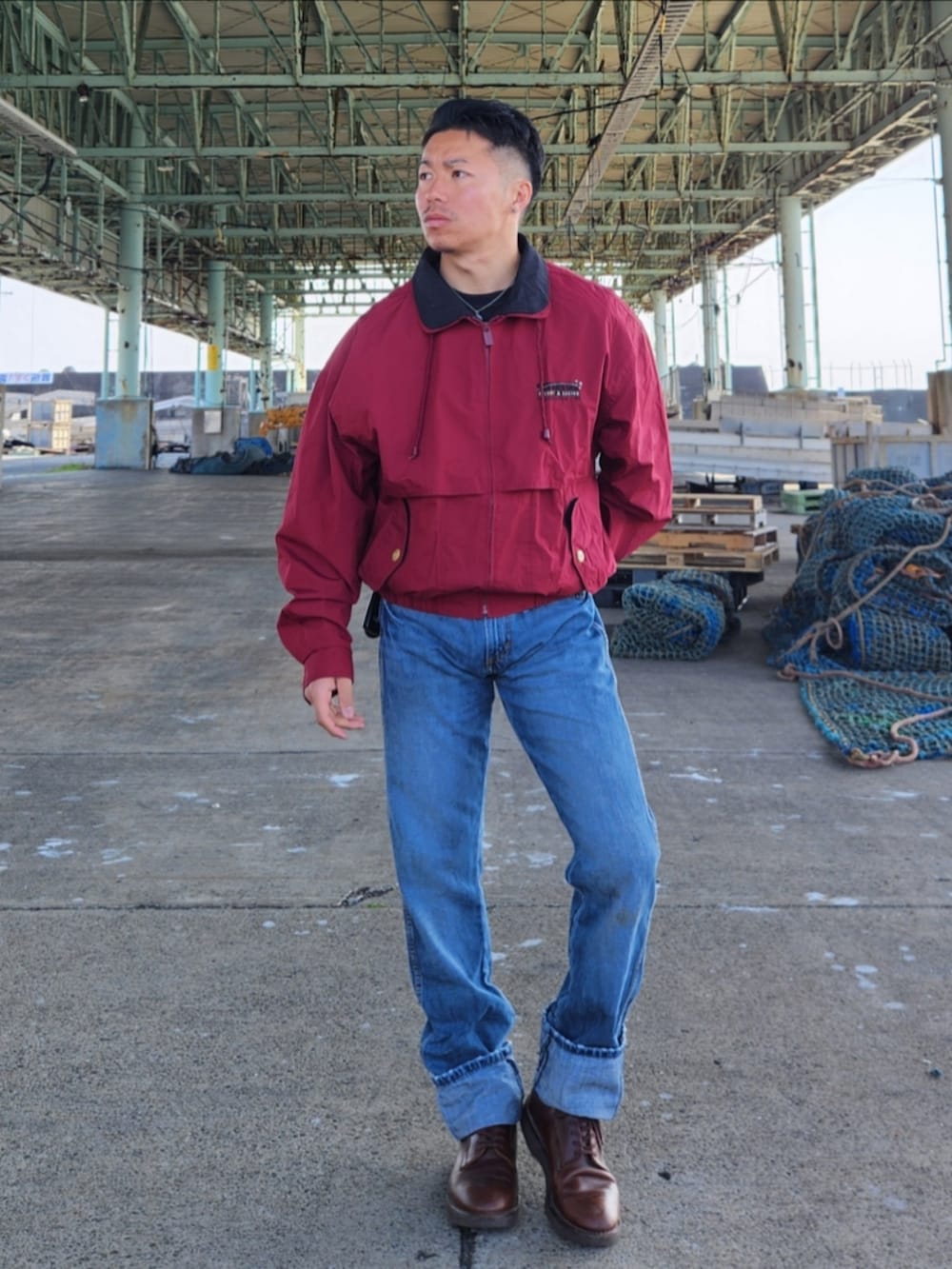 レッド系のナイロンジャケット、ブルー系のデニムパンツ、ブラウン系のブーツを着用したメンズの冬コーディネートの2枚目の写真