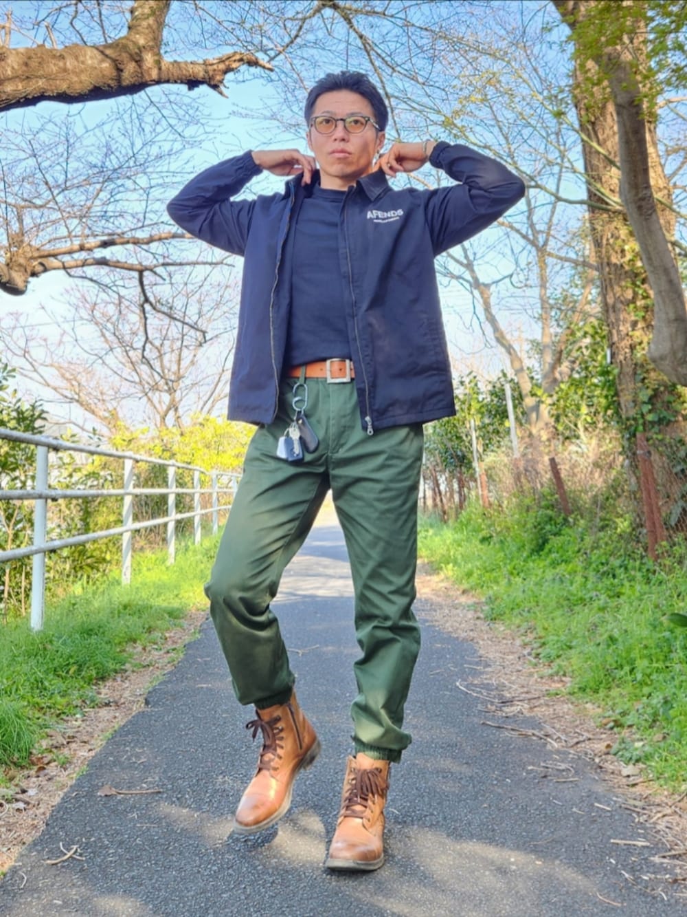 ブラウン系のブーツ、グリーン系のカーゴパンツ、ブラック系のTシャツ/カットソーを着用したメンズの春コーディネートの2枚目の写真
