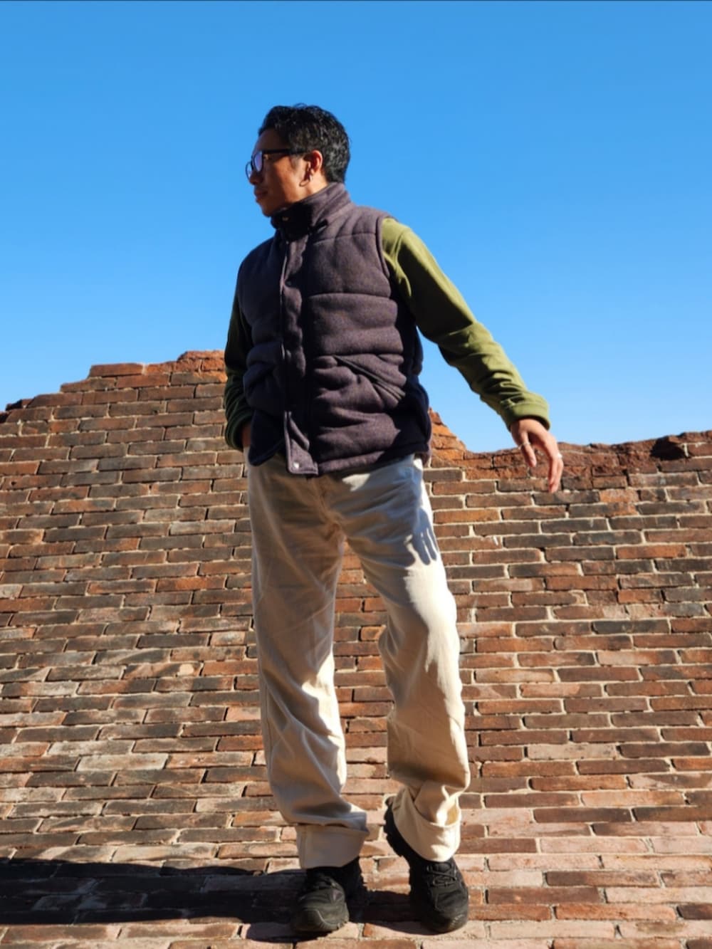 グリーン系のポロシャツ、ブラック系のダウンベスト、ホワイト系のパンツを着用したメンズの秋コーディネートの2枚目の写真