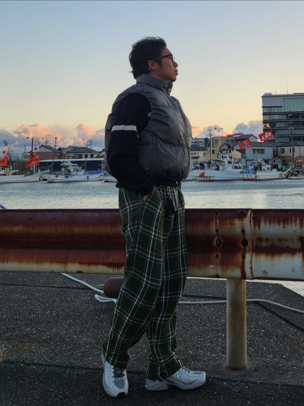 グレー系のダウンベスト、ブラック系のニット/セーター、グリーン系のパンツを着用したメンズの冬コーディネートの2枚目の写真