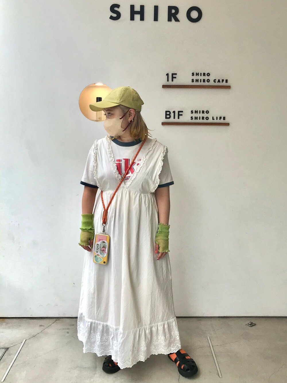 ホワイト系のワンピース、ブラック系のサンダル、オレンジ系のスマホグッズを着用したレディースの秋コーディネートの2枚目の写真