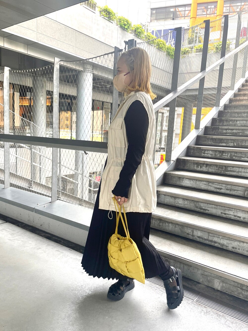 イエロー系のショルダーバッグ、ブラック系のスカート、ホワイト系のベストを着用したレディースの秋コーディネートの2枚目の写真