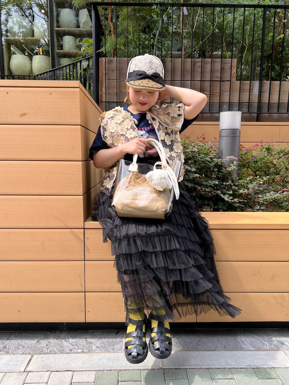 ホワイト系のトートバッグ、ベージュ系のベスト、ブラック系のサンダルを着用したレディースの夏コーディネートの2枚目の写真