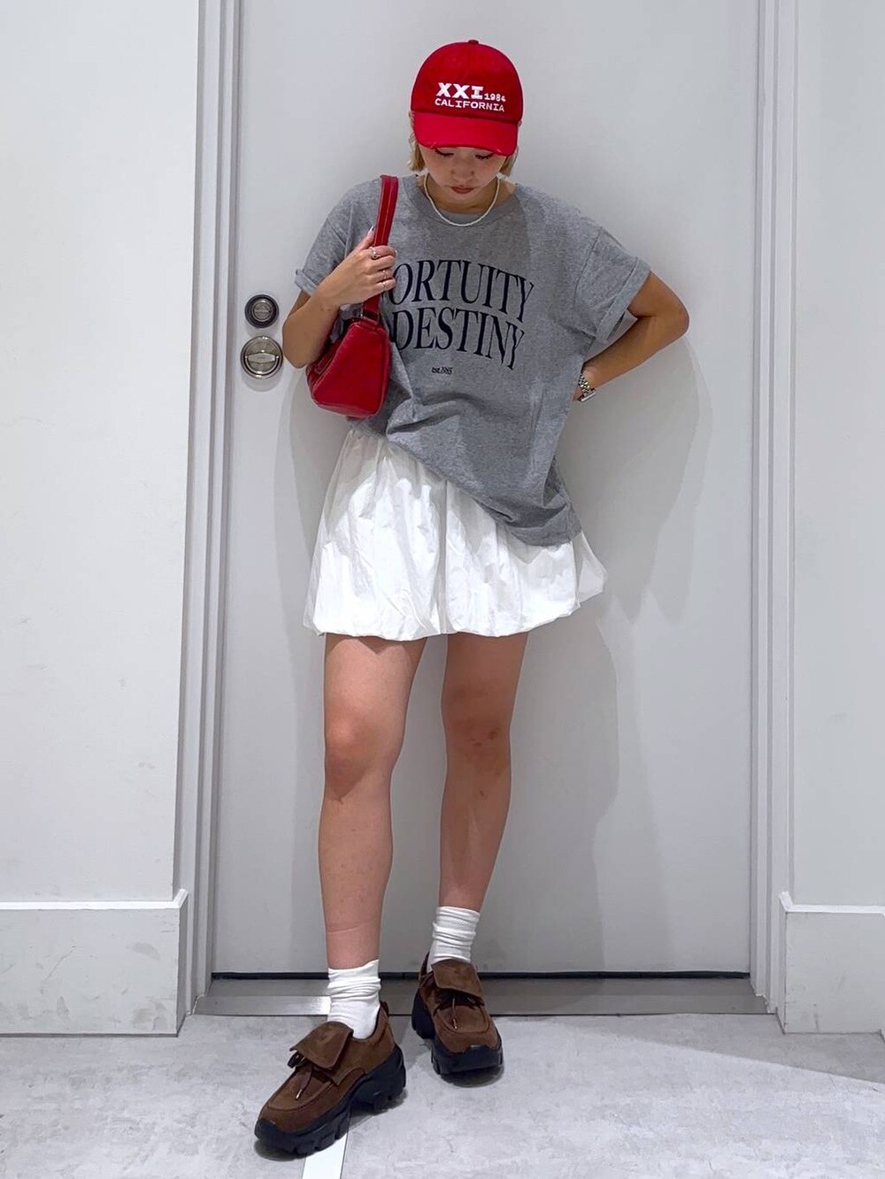 ホワイト系のスカート、ブラウン系のモカシン/デッキシューズ、グレー系のTシャツ/カットソーを着用したレディースの夏コーディネートの2枚目の写真