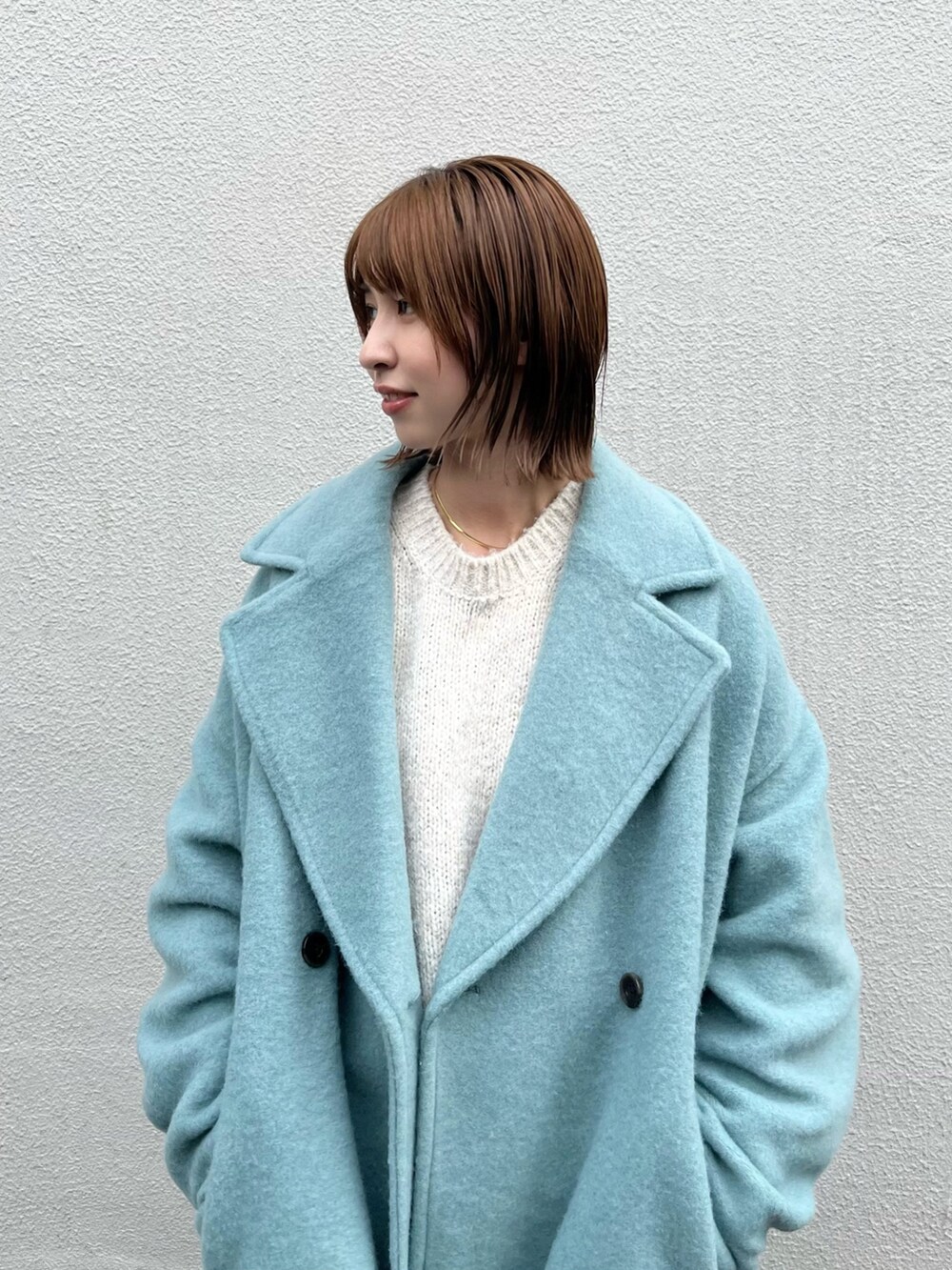 ブルー系のチェスターコート、ホワイト系のニット/セーター、ブルー系のデニムパンツを着用したレディースの秋コーディネートの4枚目の写真