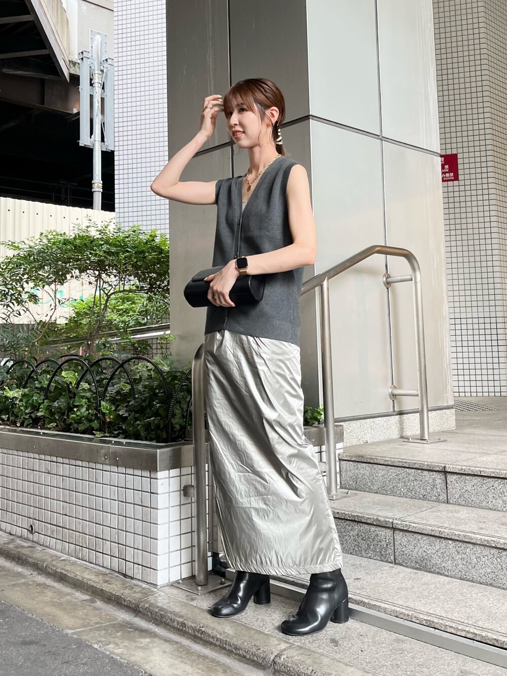 グレー系のベスト、シルバー系のスカート、ブラック系のショルダーバッグを着用したレディースの夏コーディネートの2枚目の写真