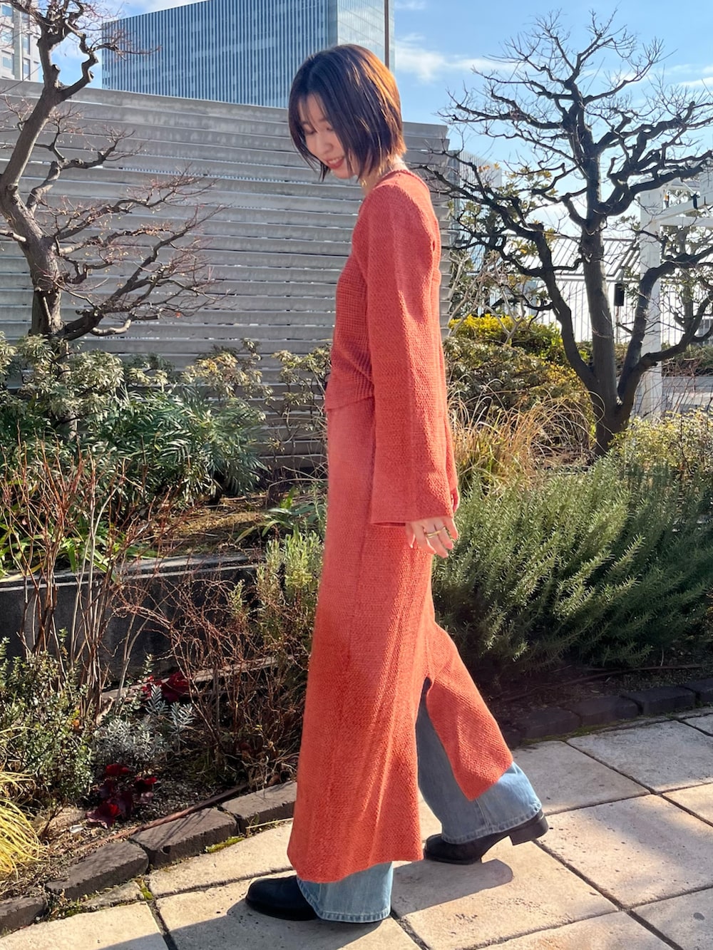 オレンジ系のワンピース、ブルー系のデニムパンツを着用したレディースの冬コーディネートの2枚目の写真