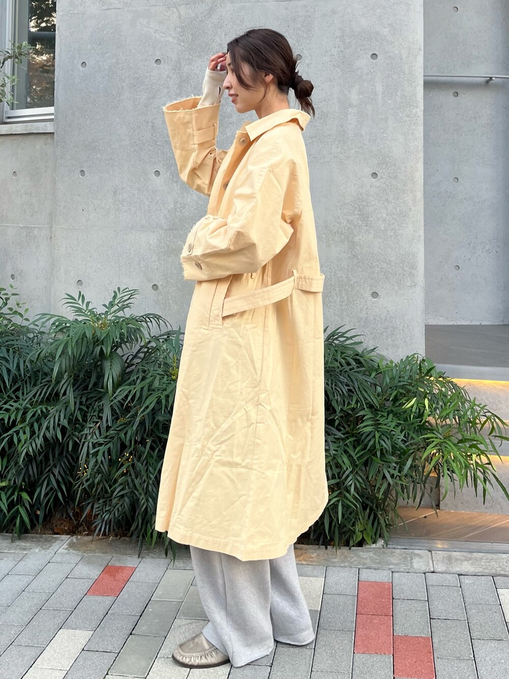 イエロー系のステンカラーコート、ホワイト系のTシャツ/カットソー、グレー系のその他パンツを着用したレディースの秋コーディネートの2枚目の写真