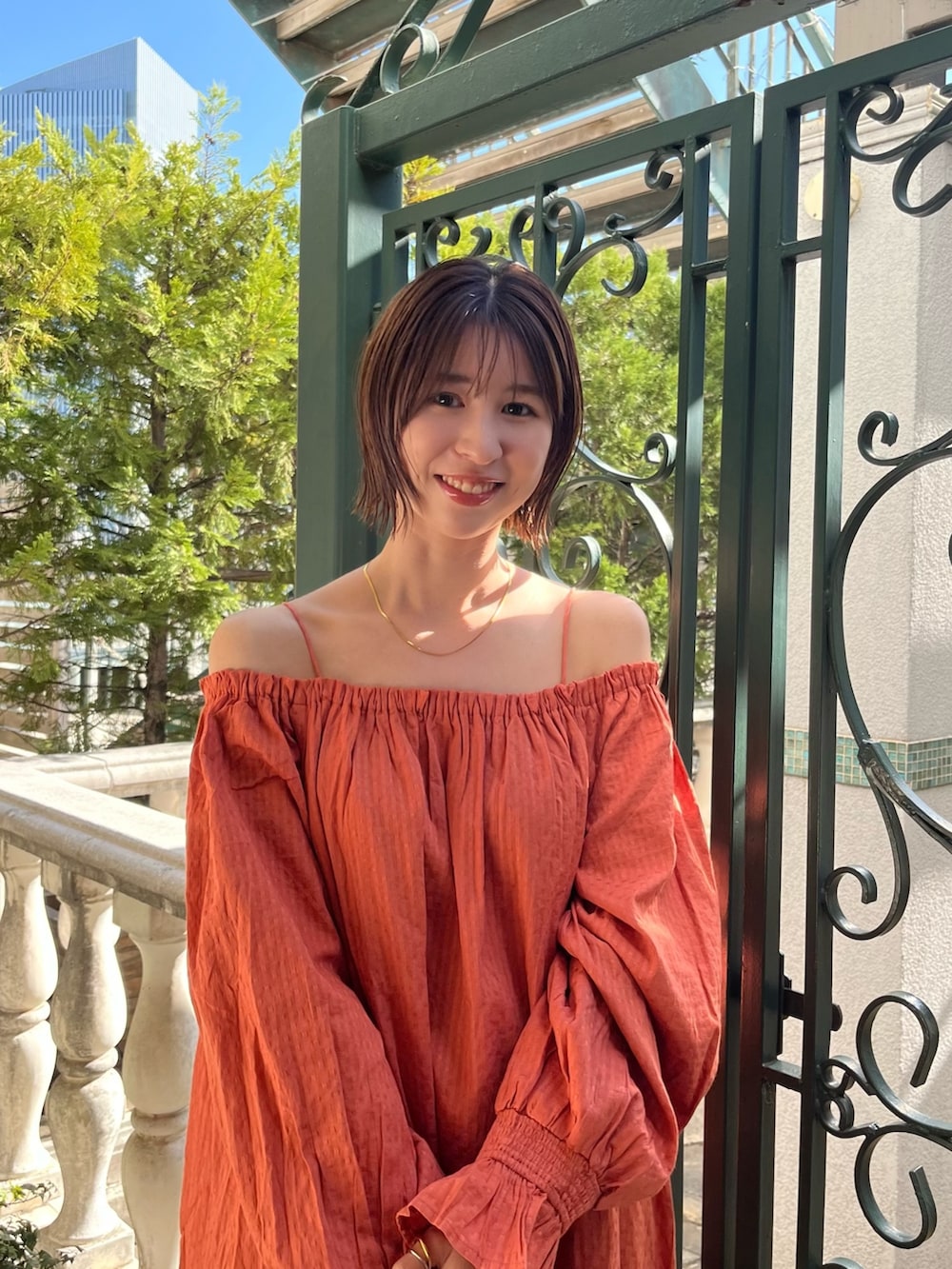 オレンジ系のワンピース、ブルー系のデニムパンツ、ゴールド系のパンプスを着用したレディースの春コーディネートの3枚目の写真