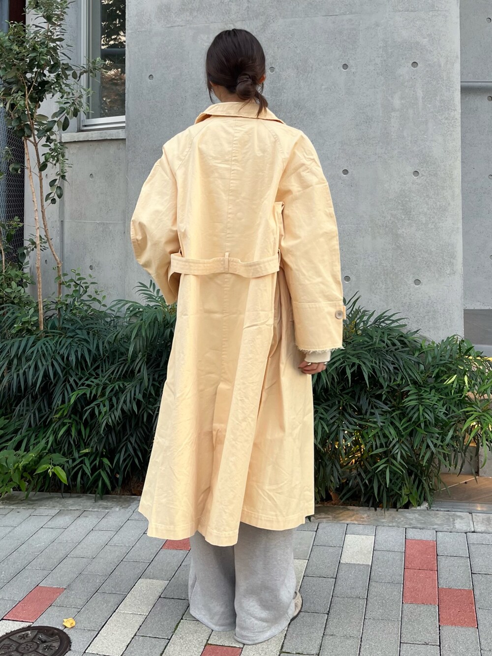 イエロー系のステンカラーコート、ホワイト系のTシャツ/カットソー、グレー系のその他パンツを着用したレディースの秋コーディネートの3枚目の写真