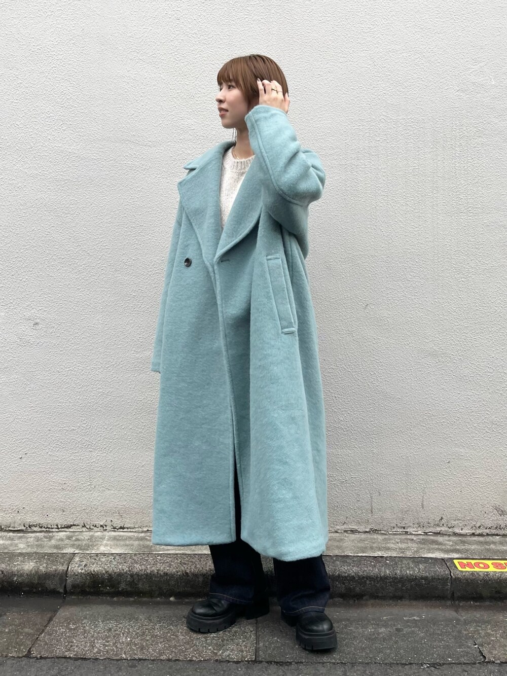 ブルー系のチェスターコート、ホワイト系のニット/セーター、ブルー系のデニムパンツを着用したレディースの秋コーディネートの2枚目の写真