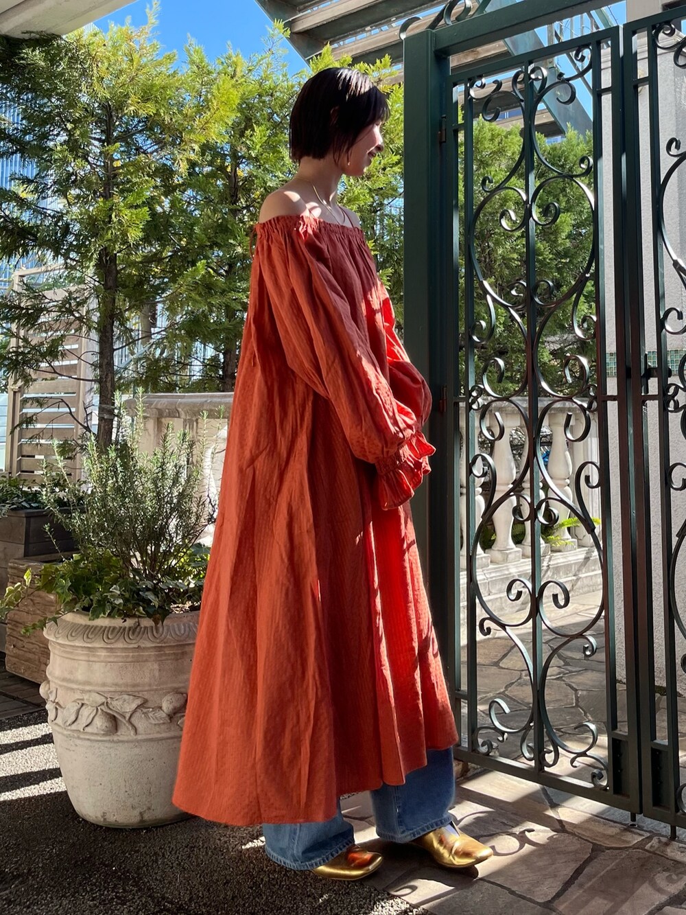 オレンジ系のワンピース、ブルー系のデニムパンツ、ゴールド系のパンプスを着用したレディースの春コーディネートの2枚目の写真