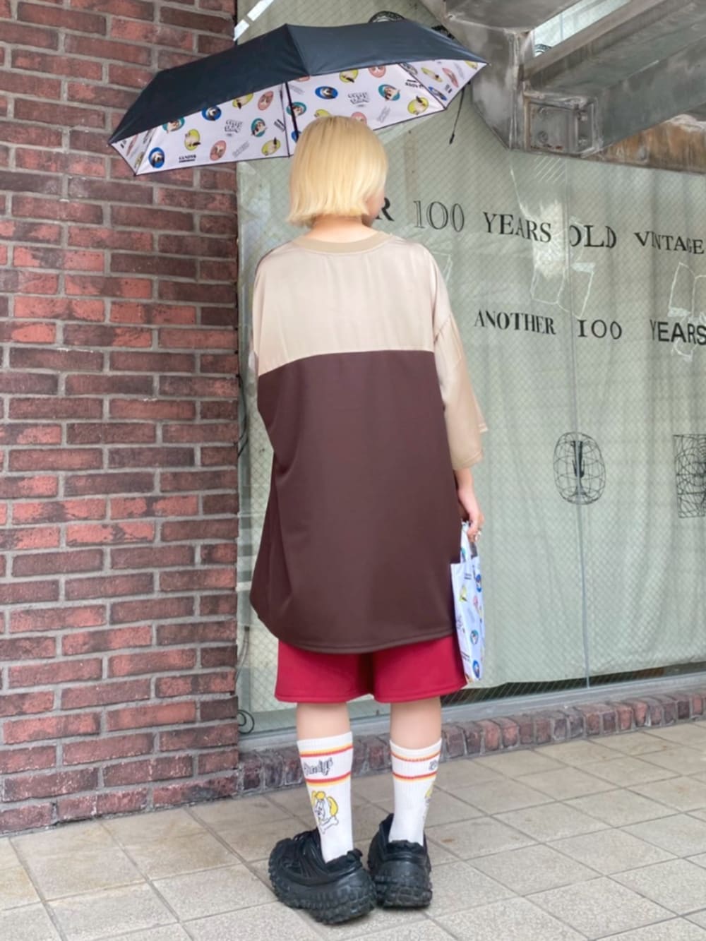 ブラウン系のTシャツ/カットソー、レッド系のその他パンツ、ブラック系の折りたたみ傘を着用したレディースの夏コーディネートの2枚目の写真