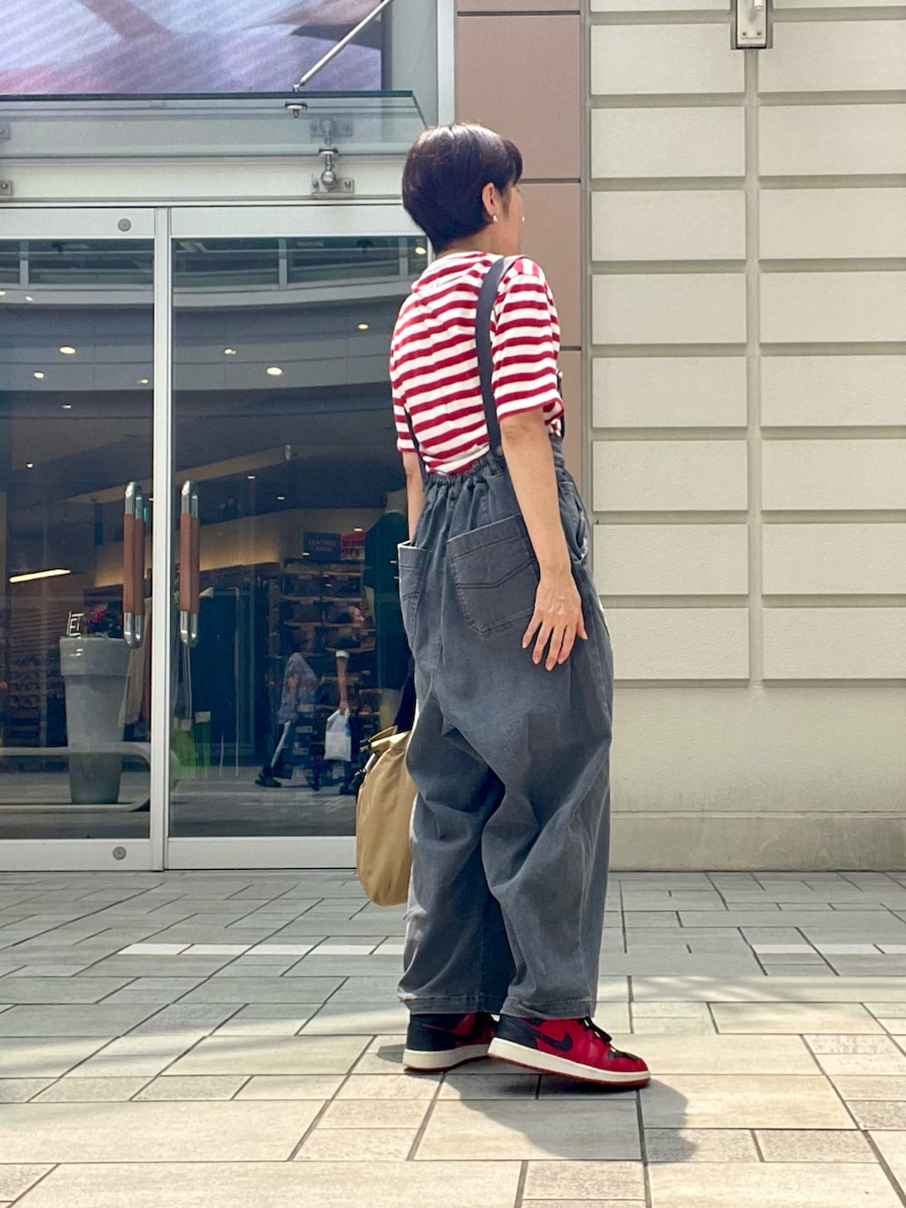 レッド系のTシャツ/カットソー、レッド系のスニーカー、グレー系のオールインワン・サロペットを着用したレディースの夏コーディネートの2枚目の写真