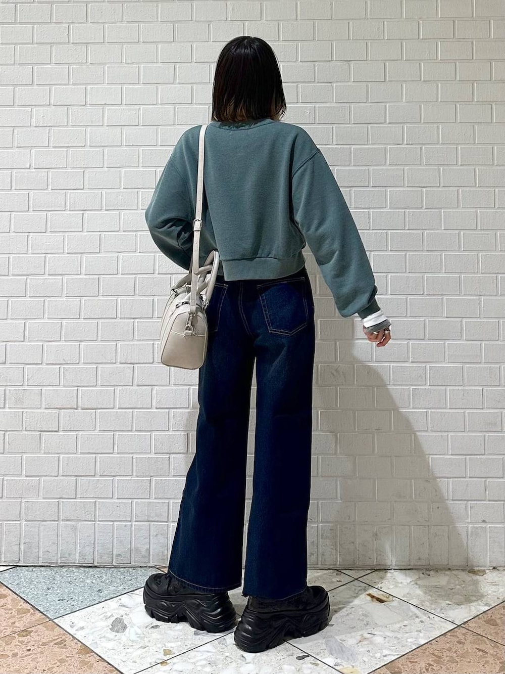 ブラック系のスニーカー、ブルー系のスラックス、ホワイト系のボストンバッグを着用したレディースの冬コーディネートの5枚目の写真