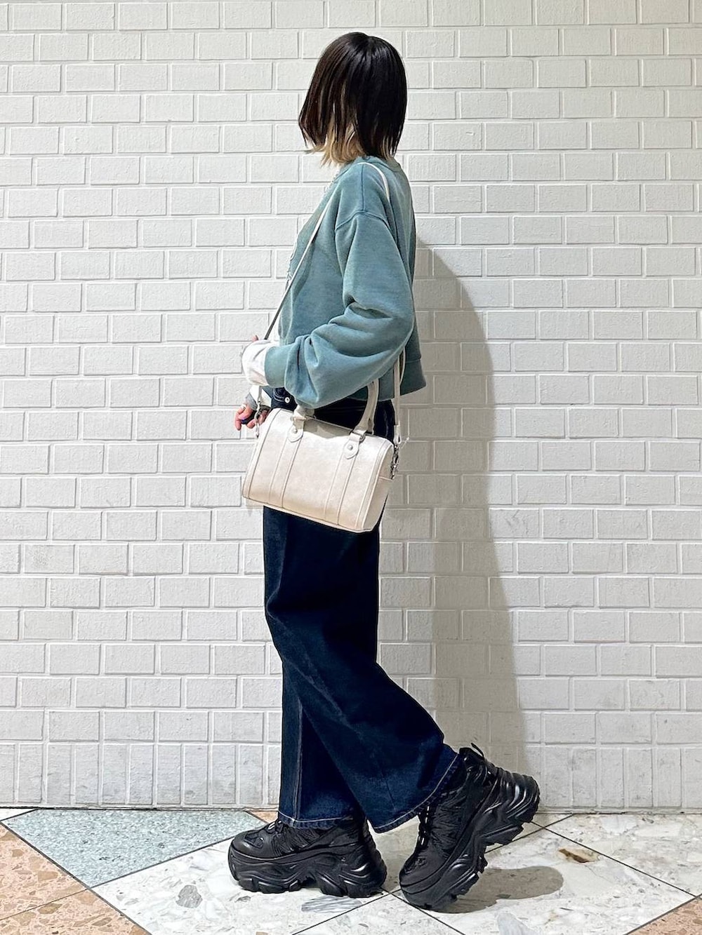 ブラック系のスニーカー、ブルー系のスラックス、ホワイト系のボストンバッグを着用したレディースの冬コーディネートの4枚目の写真