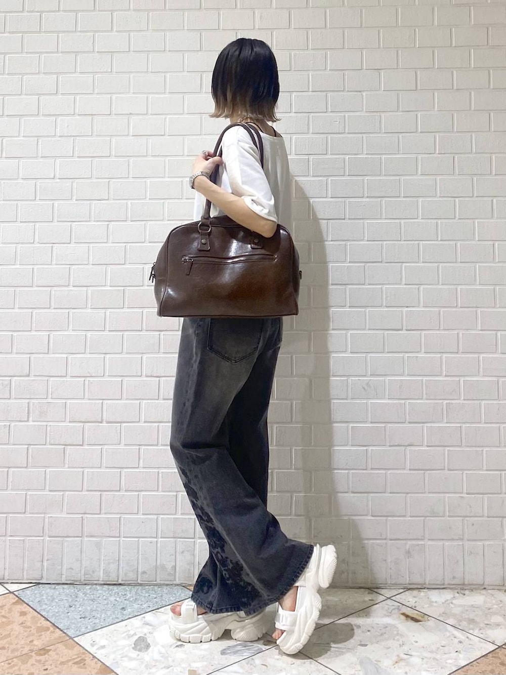 ブラウン系のボストンバッグ、ホワイト系のサンダル、ブラック系のデニムパンツを着用したレディースの春コーディネートの3枚目の写真