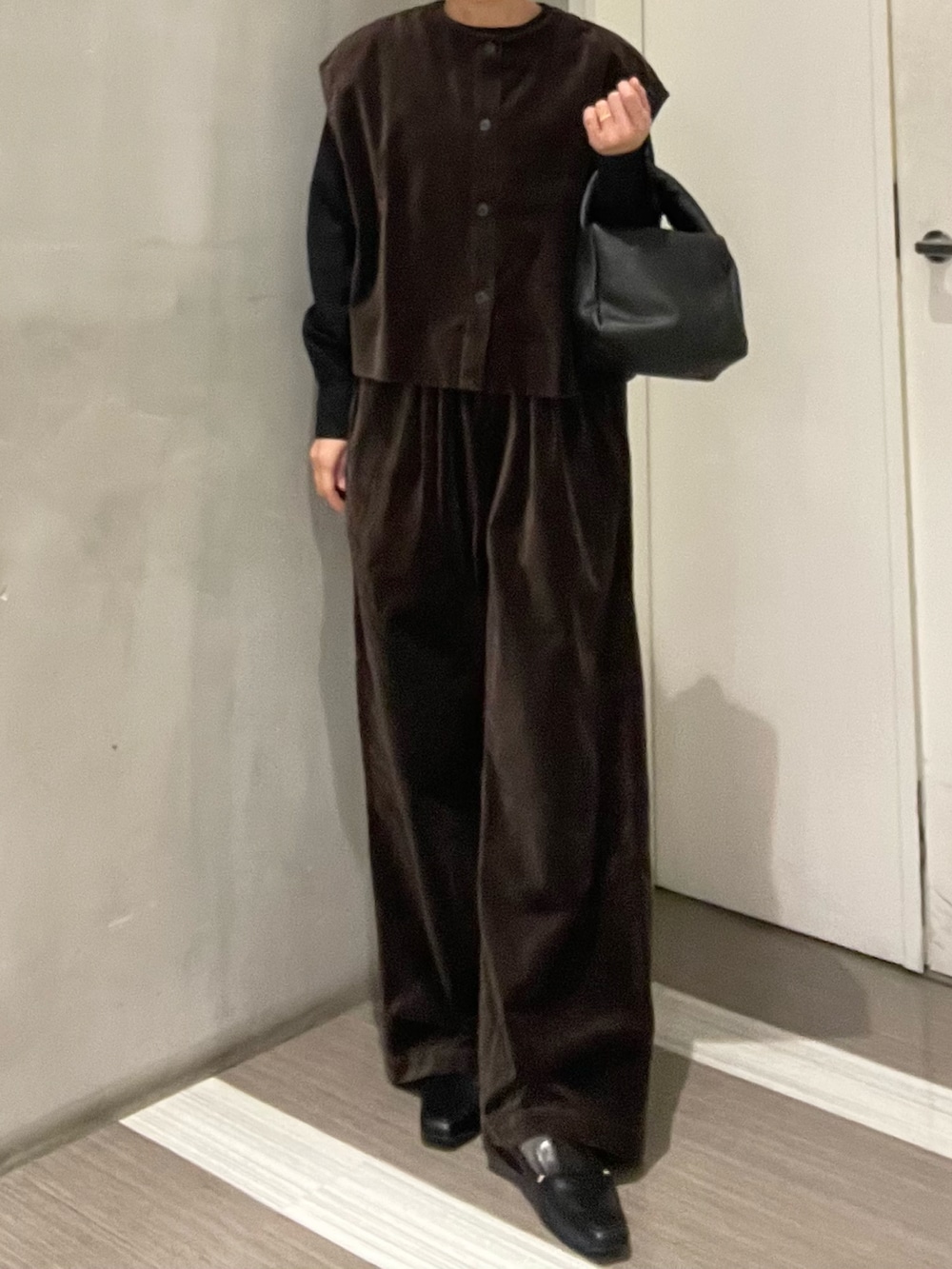 ブラック系のハンドバッグ、ブラック系のローファー、ブラウン系のベストを着用したレディースの秋コーディネートの2枚目の写真