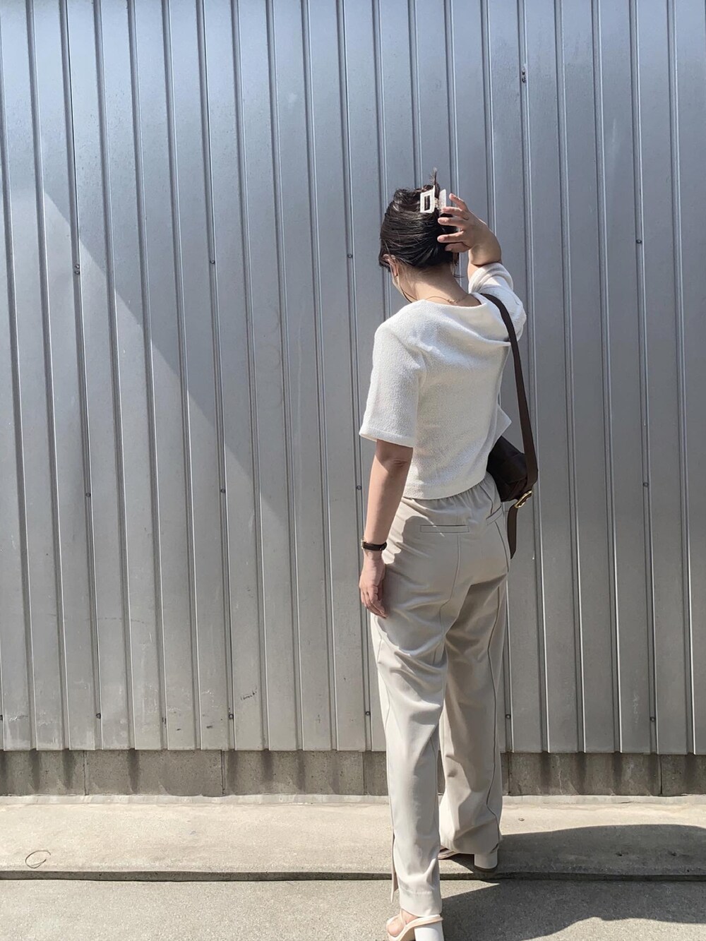 ブラウン系のショルダーバッグ、ベージュ系のスラックス、ホワイト系のサンダルを着用したレディースの夏コーディネートの2枚目の写真