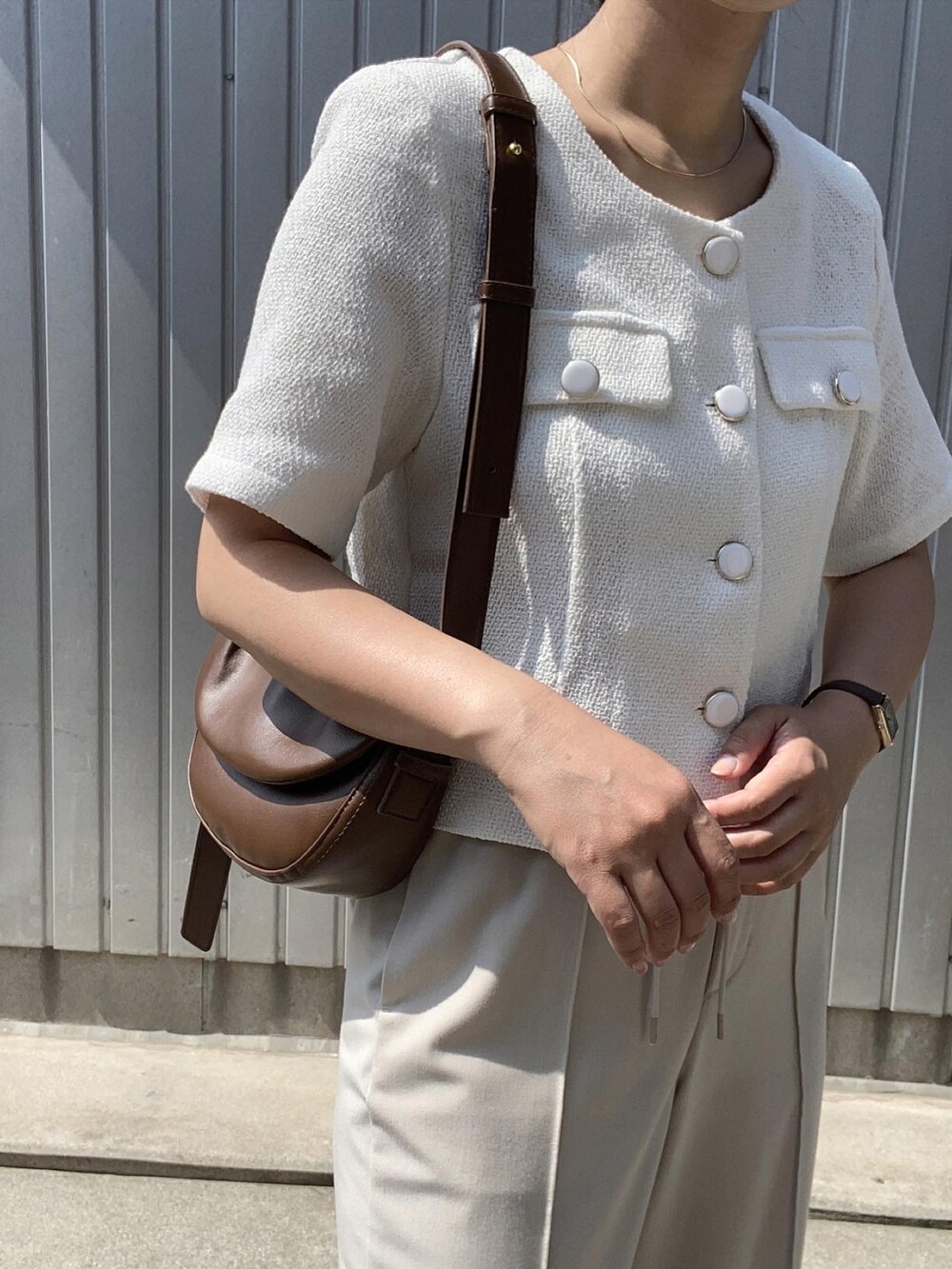 ブラウン系のショルダーバッグ、ベージュ系のスラックス、ホワイト系のサンダルを着用したレディースの夏コーディネートの3枚目の写真