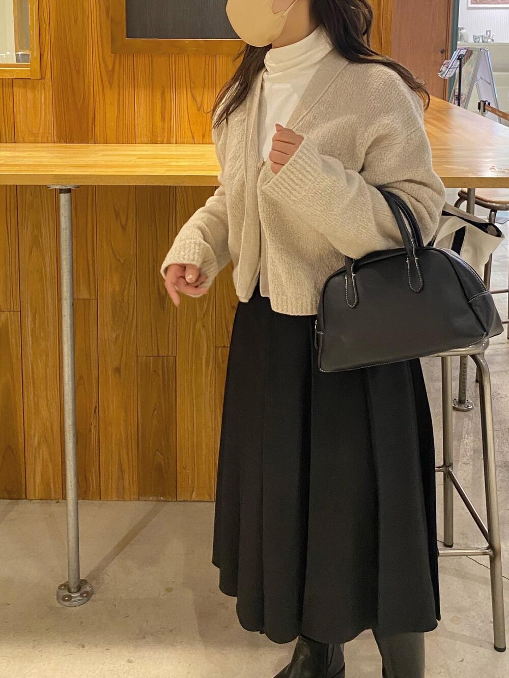 ベージュ系のカーディガン/ボレロ、ブラック系のハンドバッグ、ブラック系のブーツを着用したレディースの冬コーディネートの2枚目の写真