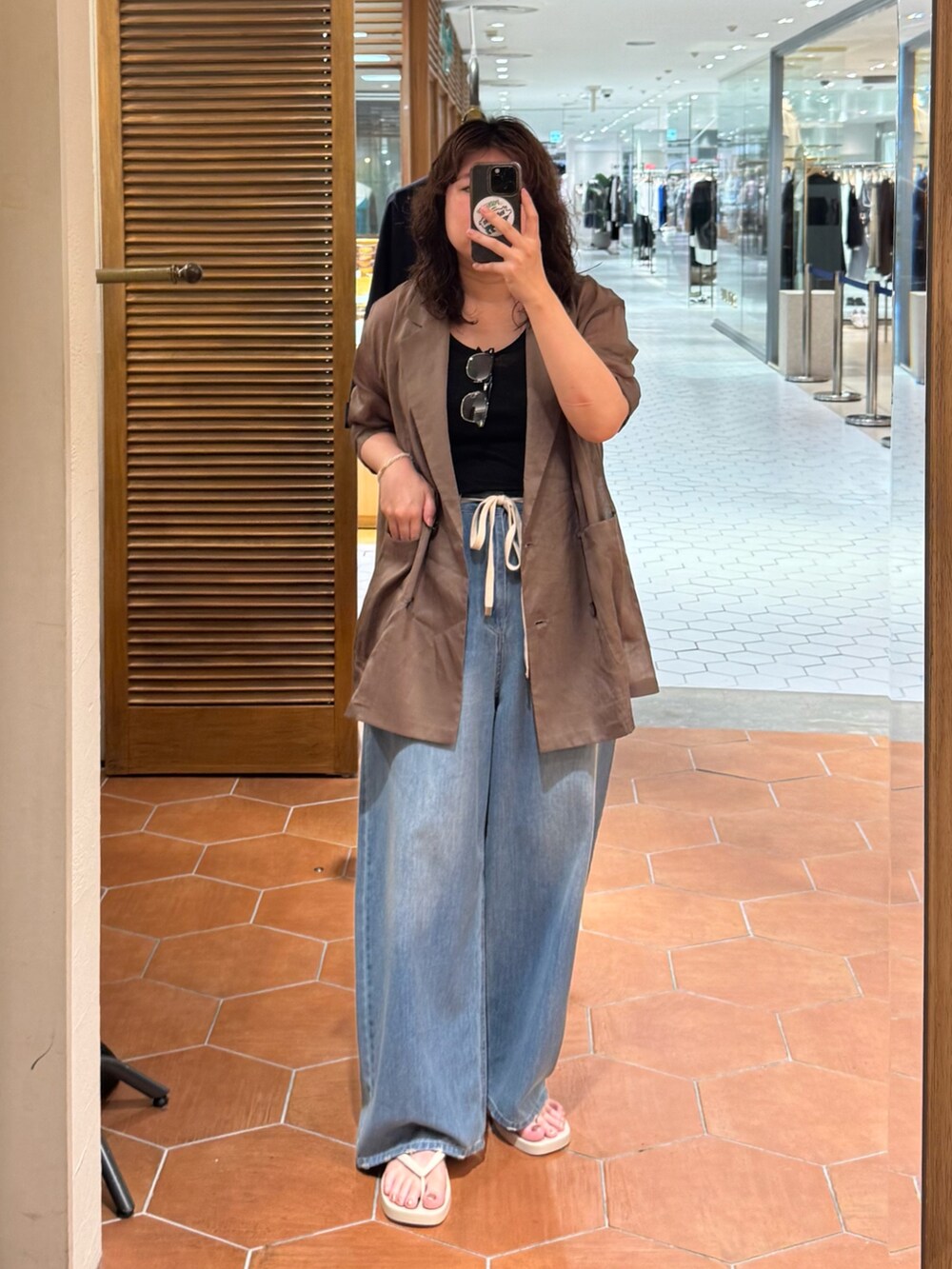 ブルー系のデニムパンツ、ブラウン系のテーラードジャケット、ホワイト系のハンドバッグを着用したレディースの夏コーディネートの2枚目の写真