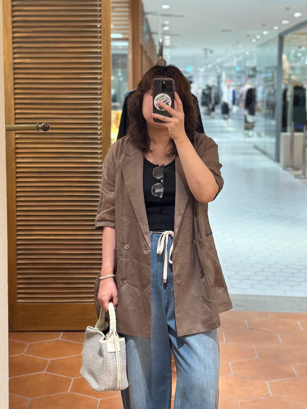 ブルー系のデニムパンツ、ブラウン系のテーラードジャケット、ホワイト系のハンドバッグを着用したレディースの夏コーディネートの3枚目の写真